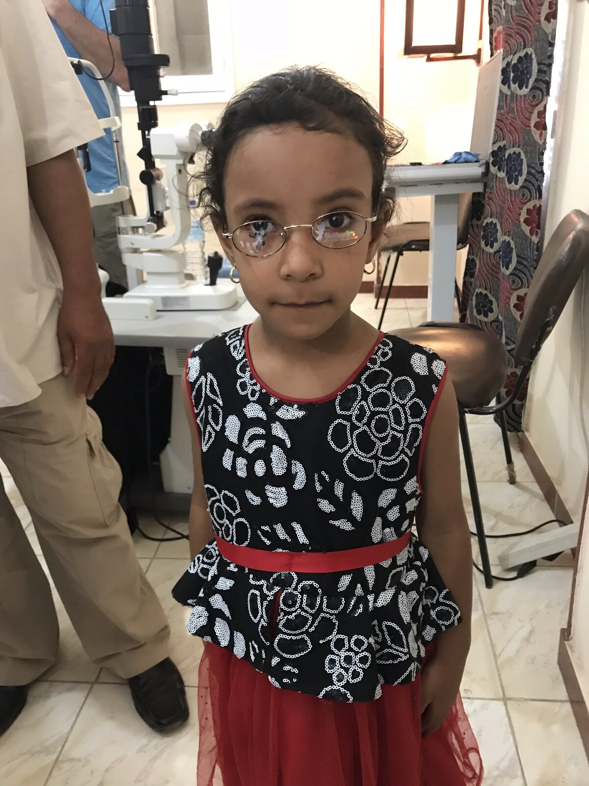 A young girl in a black, red and white floral dress wearing her new glasses