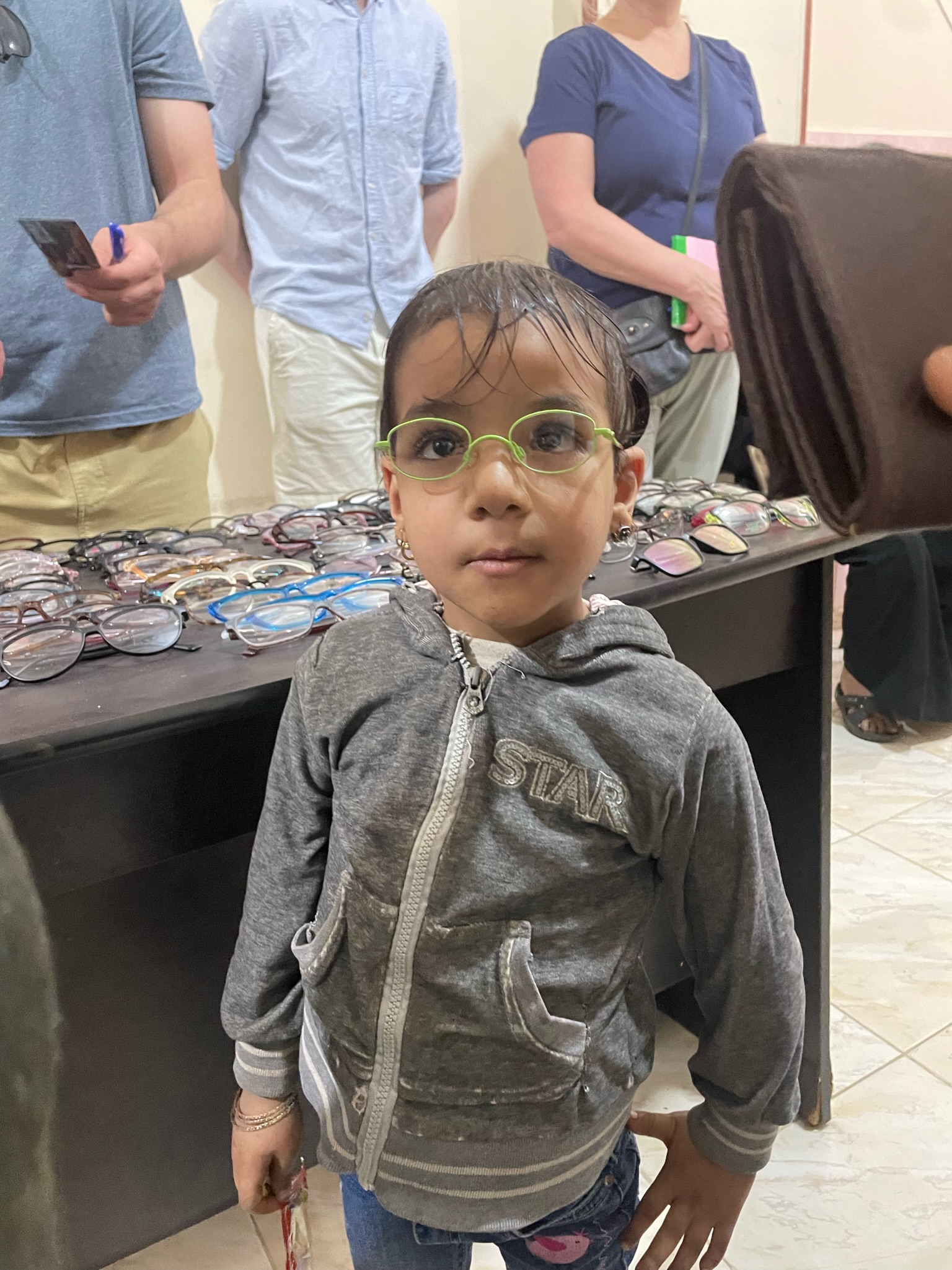 A young girl smiling in her new green glasses at the clinic