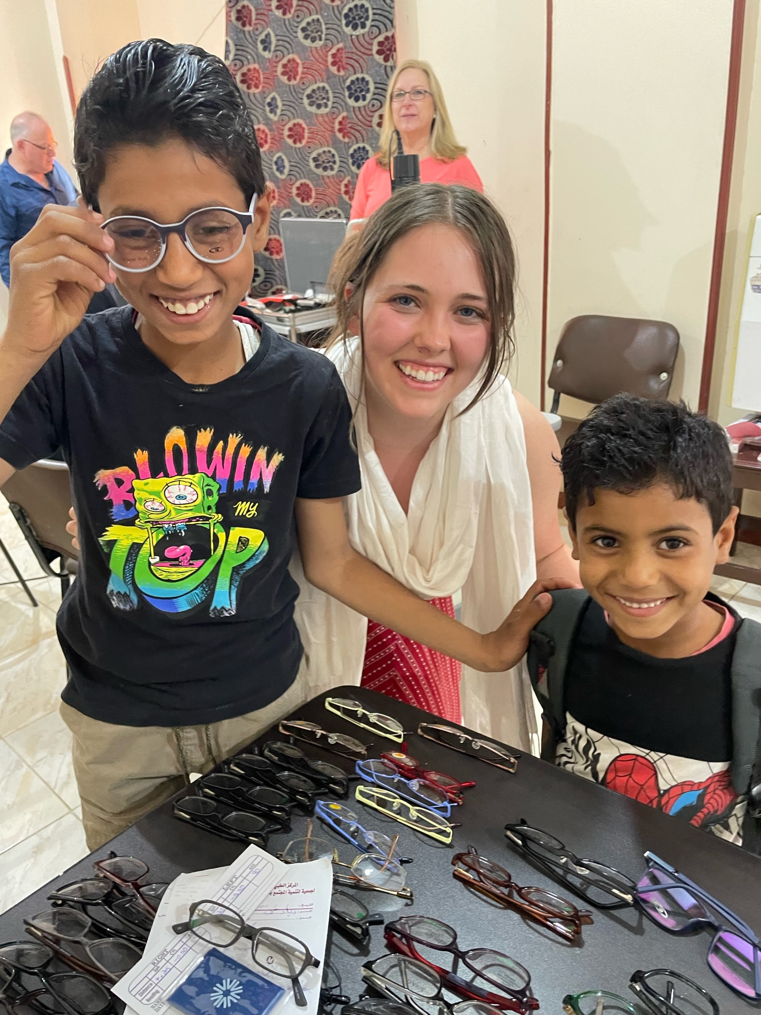 A volunteer with two boys trying on new glasses